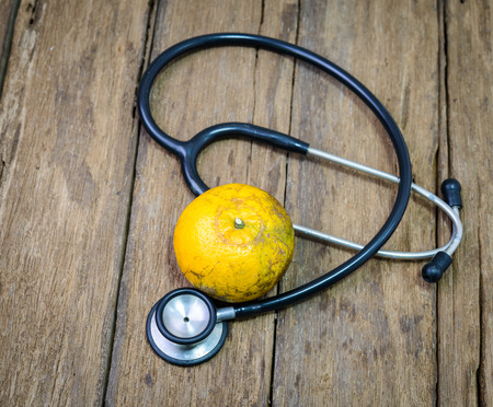 Old stethoscope and orange on wooden tableの写真素材
