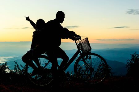 Boy with his sister riding bicycle on sunrise background.Silhouetteの写真素材
