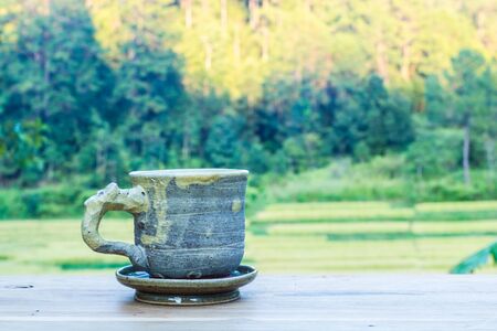 Cup of coffee on a wooden table in morning over mountain.の写真素材