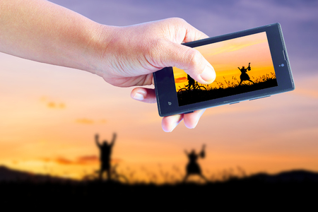 Taking pictures lChildren playing in sunset, silhouette, freedom and happiness with mobile phone in the blur nature background.の写真素材