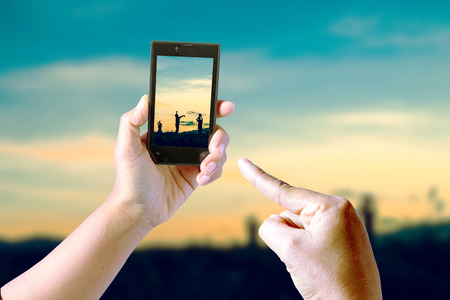 Taking pictures Children playing in sunset, silhouette, freedom and happiness with mobile phone in the blur nature background.の写真素材