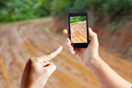 Business conceptual- Focused on right hand holding empty mobile with Trekking road mud  blurred backgroundの写真素材