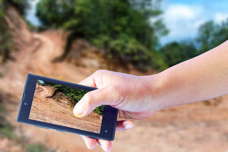 Business conceptual- Focused on right hand holding mobile with Trekking dirt road blurred backgroundの写真素材