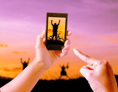 Taking pictures Children playing in sunset, silhouette, freedom and happiness with mobile phone in the blur nature background.の写真素材