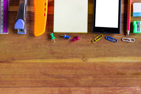 Assorted Office Supplies such as notebooks, cutter, mobile phones, Thumbtacks and Clips on Top of Wooden Desk with Copy Space.の写真素材