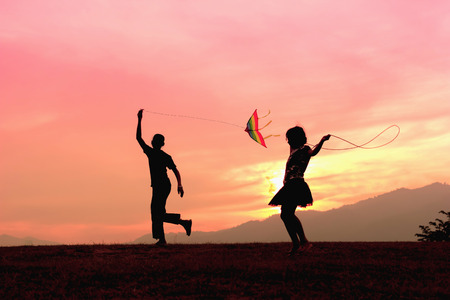 A brother getting a kite to fly and sister rope jumping during sunset.の写真素材