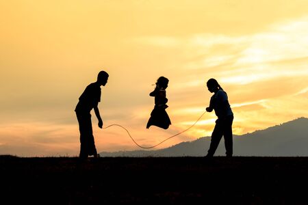 silhouetted children rope skipping in sunsetの写真素材