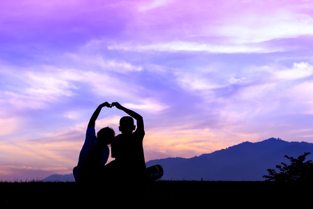 Silhouette young brother and sister made a heart shape, Beautiful sunset and skyの写真素材
