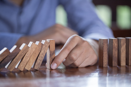 Businessman stopping domino effect with his finger. Business crisis concept.の写真素材