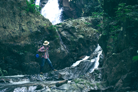 Backpacker looking at waterfall in beautiful summer nature landscape. Portrait of male adult back standing outdoor.の写真素材