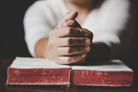 Woman hands praying with a bible in a dark over wooden table