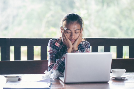 Young woman sitting in front of laptop, looking at screen with frustrated expression, holding her head in hands, having headache, low or high arterial blood pressure, stressの写真素材