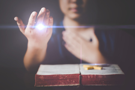 Woman praying on holy bible in the morning. Teenager woman hand with Cross and Bible praying, Hands folded in prayer on a Holy Bible in church concept for faith, spirituality and religion.の写真素材