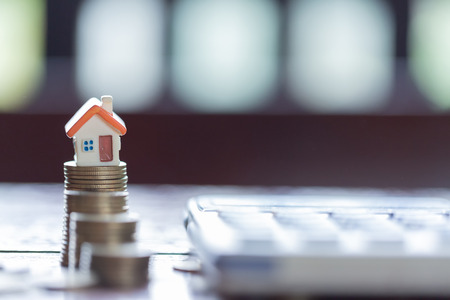 House model and coins stacks with calculator as background. Concept for property ladder, mortgage and real estate investment.の写真素材