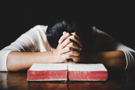 Woman hands praying with a bible in a dark over wooden tableの写真素材