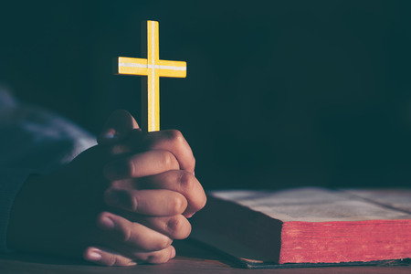 Young teen girl holding a cross praying with hands close up, vintage effect, soft focus.