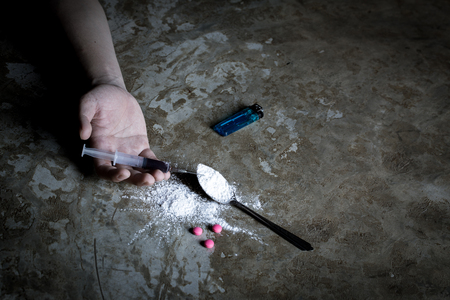 International Day against Drug Abuse. Young human hand trying to reach cooked heroin spoon on grungy concrete floor. Drugs addiction and withdrawal symptoms concept. Copy space.の写真素材