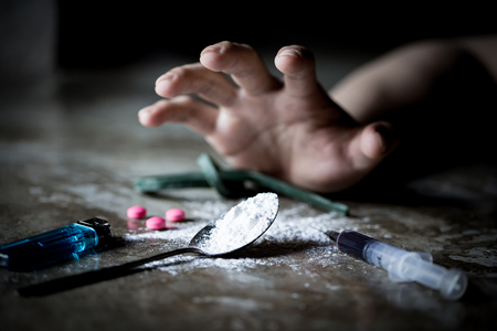 International Day against Drug Abuse. Young human hand trying to reach cooked heroin spoon on grungy concrete floor. Drugs addiction and withdrawal symptoms concept. Copy space.の写真素材