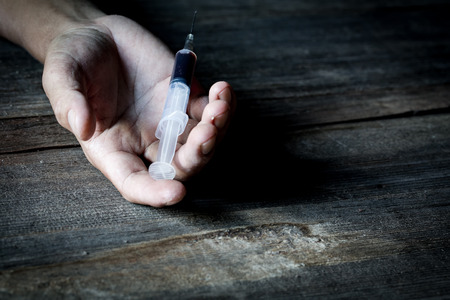 Drug abuse concept, overdose male drug addict hand, drugs narcotic syringe in hand on the floorの写真素材