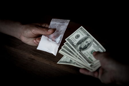 Hand of addict man with money buying dose of cocaine or heroine or another narcotic from drug dealer. Drug abuse and traffic concept.の写真素材