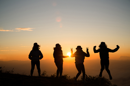 Silhouette of young woman are standing on top of the mountain relaxing with sunrise by nature at sunrise, Life style, Group of happy at sunrise or sunset, First morning lightの写真素材