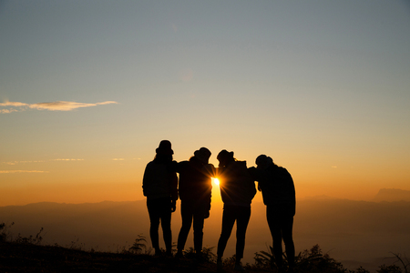 Silhouette of young woman are standing on top of the mountain relaxing with sunrise by nature at sunrise, Life style, Group of happy at sunrise or sunset, First morning lightの写真素材