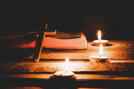 Cross with bible and candle on a old oak wooden table. Beautiful gold background. Religion concept.の写真素材