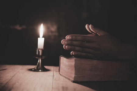 Close up man's hand is praying in the Church with lit candle, religion and faith conceptの写真素材