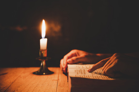Religious man reading the Holy Bible with lit candles and praying in the Church, religion and faith conceptの写真素材