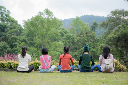Group of friends sitting together on greensward and enjoying themselves. Young women enjoying on their holiday outdoors.の写真素材