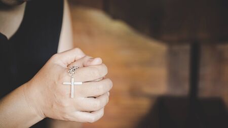 Closeup of christian senior woman hands holding crucified cross while praying God.