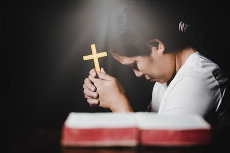 Woman hands praying with a cross and bible in a dark over wooden tableのeditorial素材