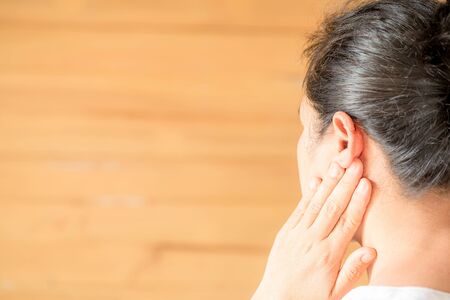 Female having ear pain touching his painful head on light brown backgroundの写真素材