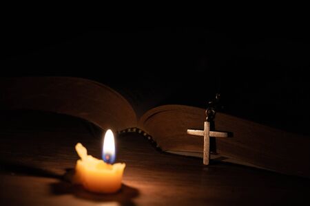 Bible, wood Cross and candles on an old wooden table with a dark background