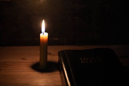 Bible and candle on a old oak wooden table. Beautiful gold background.Religion concept.