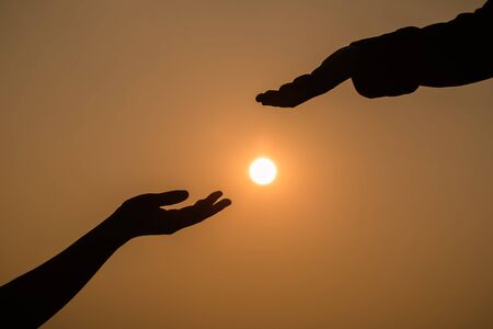 Giving a helping hand on the background of the sunset. Silhouette of helping hand concept and international day of peace. の写真素材