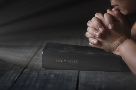 Praying hands of the woman on burred page of and old bible over wooden table backgroundの写真素材