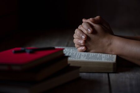 Praying hands of the woman on burred page of and old bible over wooden table backgroundの写真素材