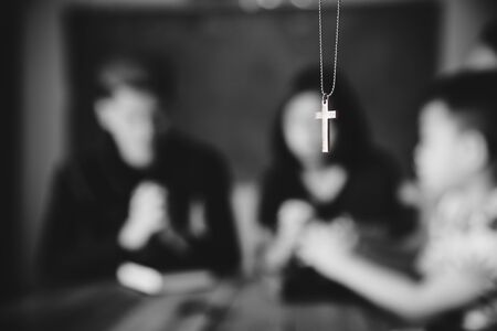Silver cross in the necklace with praying family background. Man, woman and child.