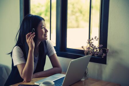 Happy young asia business woman entrepreneur using computer working in internet sit at office desk, smiling female professional employee typing email on laptop at workplaceの写真素材