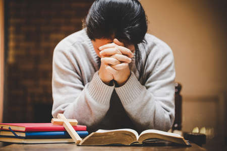Mother and son praying and praising God at home, sitting on wooden sofa in living roomの写真素材