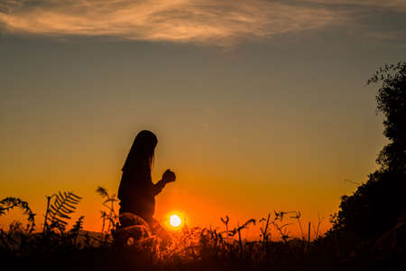 The girl bowed and prayed at sunset in the mountains, Eucharist Therapy Bless God Helping Repent Catholic Easter Lent Mind Pray. Christian Religion concept background. fighting and victory for godの写真素材