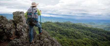 Young female tourist with backpack relaxing on top rock and enjoying view of mountainsの写真素材