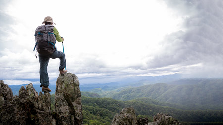 Young female tourist with backpack relaxing on top rock and enjoying view of mountains