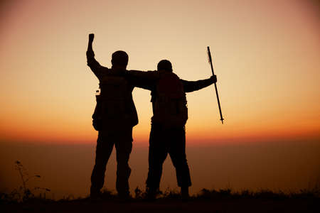 Hiker with backpack relaxing on top of a mountain and enjoying valley view during sunriseの写真素材