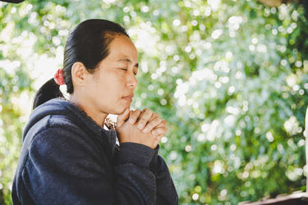 portrait of a young woman praying in nature, the girl thanks God with her hands folded at her chin, a conversation with the Creator, the concept of religionの写真素材