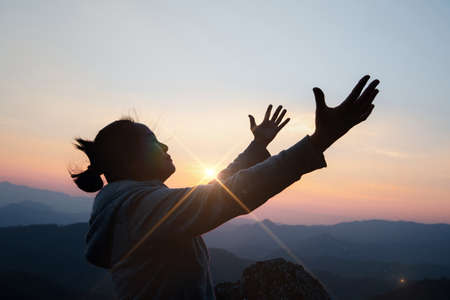Silhouette woman on sunset background. Woman raising his hands in worship. Christian Religion concept background.の写真素材