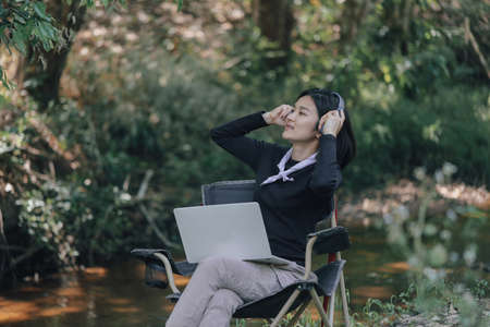 Happy woman with wireless headset using laptop in natureの写真素材