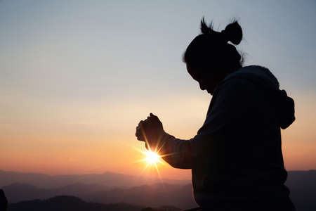 Silhouette woman on sunset background. Woman raising his hands in worship. Christian Religion concept background.の写真素材
