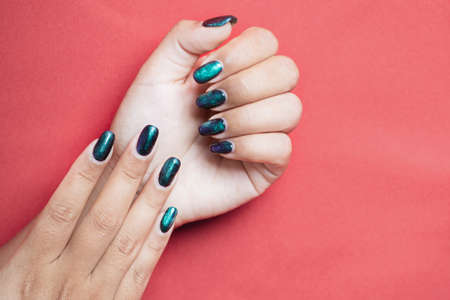 Closeup of beautiful groomed woman's hands with green spring summer nail design on red background. Manicure, pedicure beauty salon concept. copy space for text. Long nails with swamp - gel polish.の写真素材